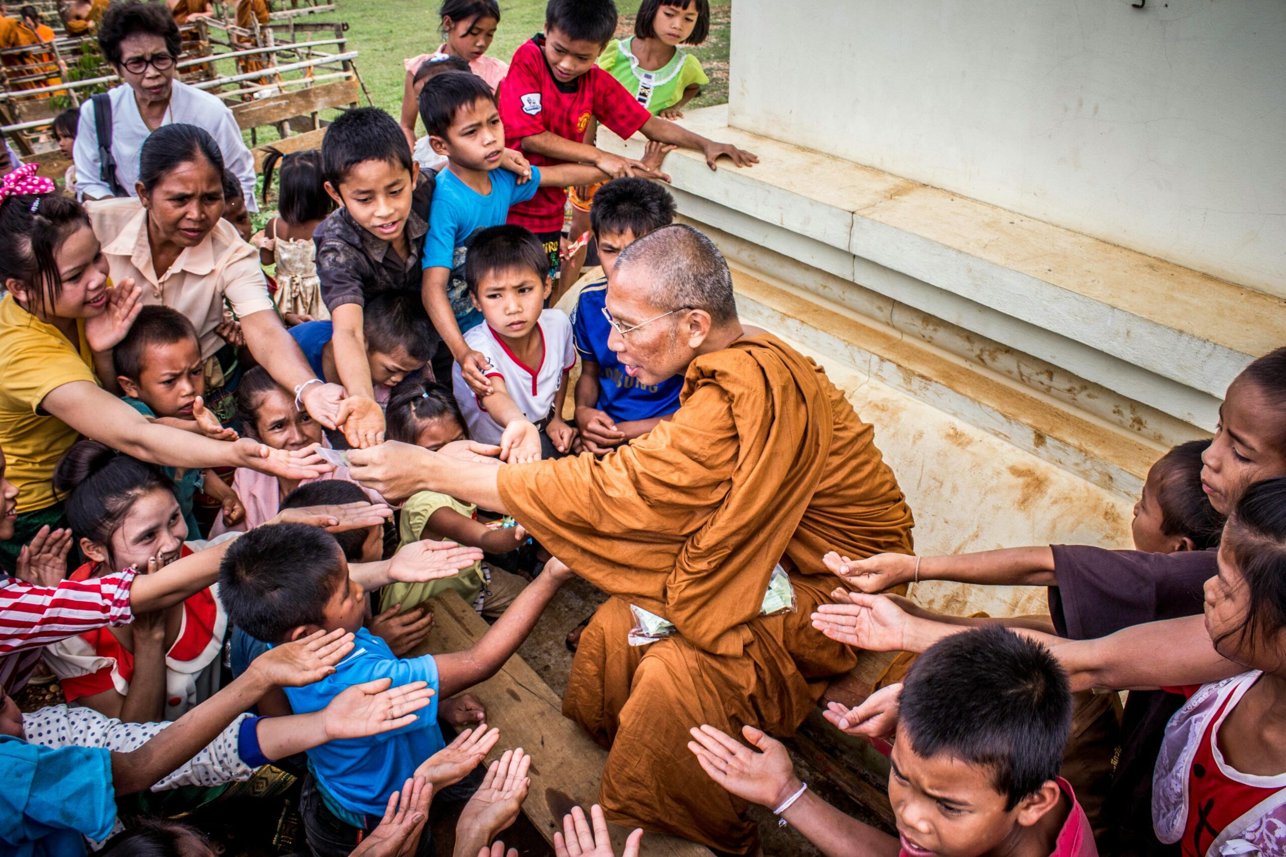 A Buddhist monk sharing gifts with children, capturing a moment of compassion and cultural tradition.